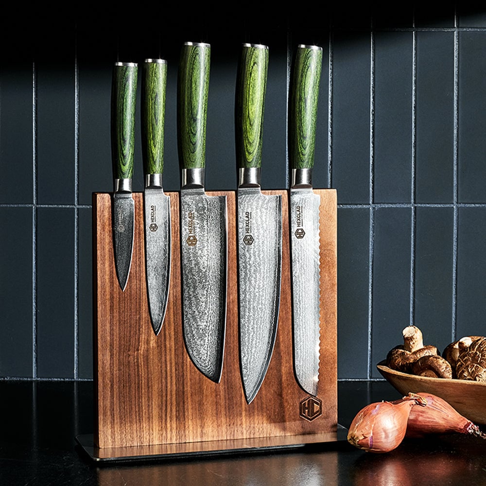 Five kitchen knives in a wooden block with green handles on a dark countertop.