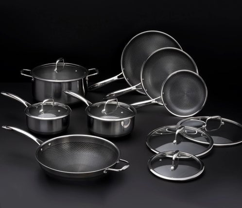 Set of stainless steel pots and pans with glass lids on a dark background.